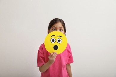 Little girl covering face with shocked emoji on white background