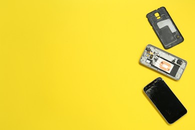 Damaged smartphone on yellow background, flat lay with space for text. Device repairing