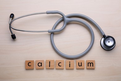 Photo of Word Calcium made of cubes with letters and stethoscope on wooden table, top view