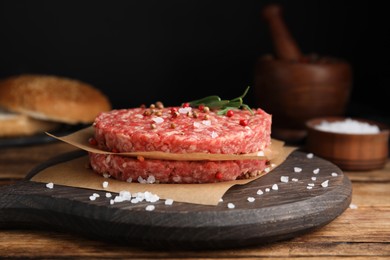 Raw hamburger patties with rosemary and spices on wooden table, closeup