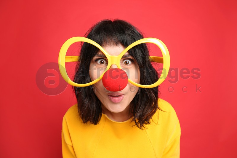 Funny woman with large glasses and clown nose on red background. April fool's day