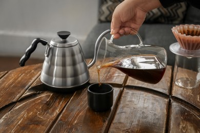 Photo of Barista pouring coffee into cup at wooden table in cafe, closeup
