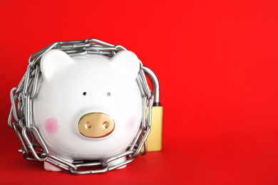 Piggy bank  with steel chain and padlock on red background, space for text. Money safety concept