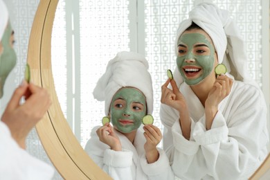 Young mother and her daughter with facial masks near mirror in bathroom