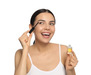 Young woman applying oil onto eyelashes on white background