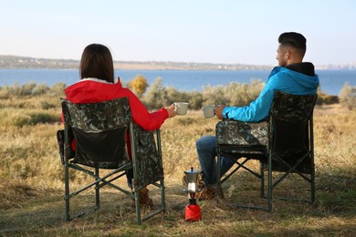 Photo of Couple resting in camping chairs and enjoying hot drink outdoors, back view
