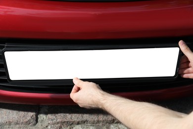 Man installing vehicle registration plate outdoors, closeup. Mockup for design