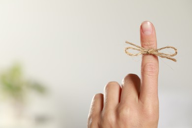 Woman showing index finger with tied bow as reminder indoors, closeup. Space for text