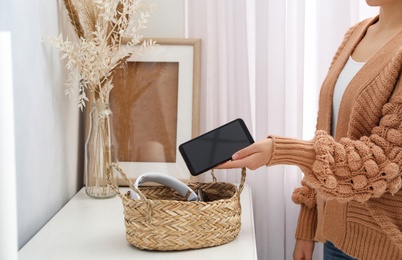 Woman putting smartphone into wicker basket with gadgets at home. Digital detox concept