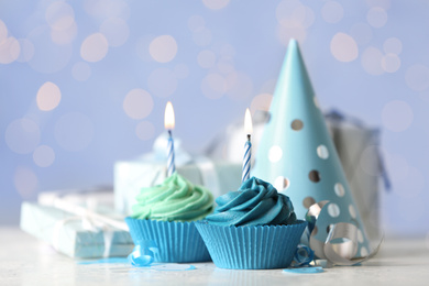 Delicious birthday cupcakes with cream and burning candles on white table