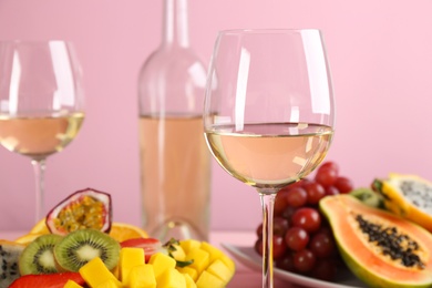 Delicious exotic fruits and glasses of wine on pink background, closeup