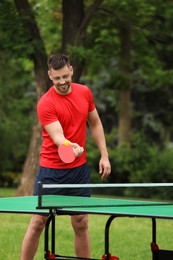 Happy man playing ping pong outdoors on summer day