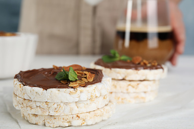 Puffed rice cakes with chocolate, nuts and mint on white wooden table, closeup. Space for text