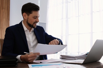 Businessman looking at wristwatch while working with documents in office