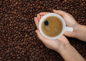 Image of Woman with cup of tasty espresso and roasted coffee beans, top view. Space for text
