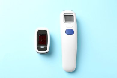Photo of Modern fingertip pulse oximeter and non contact infrared thermometer on light blue background, flat lay