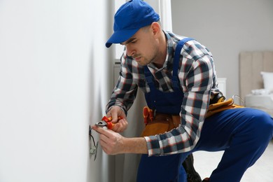 Photo of Electrician with pliers repairing power socket indoors