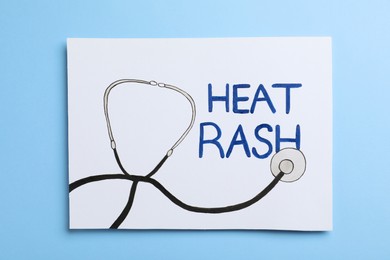 Sheet of paper with words Heat Rash and drawn stethoscope on light blue background, top view