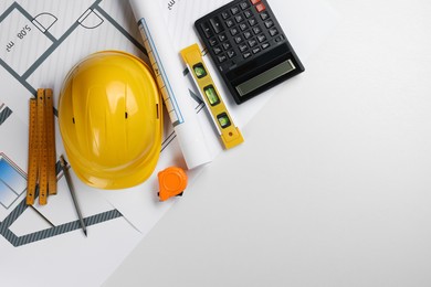 Construction drawings, safety hat, calculator, tape measure, folding ruler and bubble level on white background, top view. Space for text