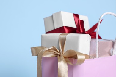 Photo of Pink paper shopping bag full of gift boxes on light blue background, closeup. Space for text