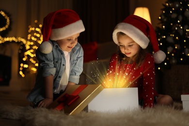 Cute children opening gift box in room decorated for Christmas
