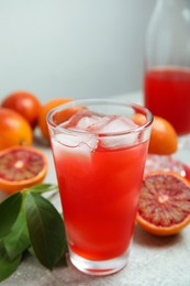 Tasty sicilian orange juice with ice cubes in glass and fruits on light grey table
