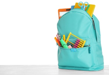 Stylish backpack with different school stationary on wooden table against white background