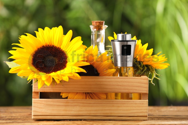 Crate with bottles of cooking oil and sunflowers on wooden table against blurred background