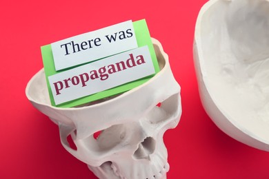 Photo of Information warfare concept, media propaganda influence. Paper card inside human skull on red background
