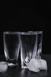 Vodka in shot glasses with ice on table against black background