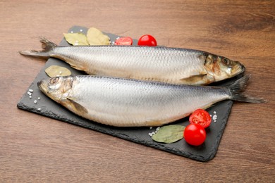 Photo of Slate plate with salted herrings, bay leaves and cherry tomatoes on wooden table
