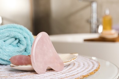 Photo of Rose quartz gua sha tool, natural face roller and towel on table in bathroom, closeup. Space for text