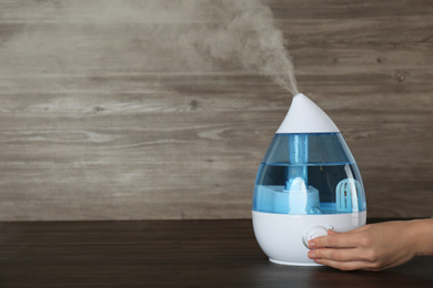 Woman using modern air humidifier at wooden table, closeup. Space for text