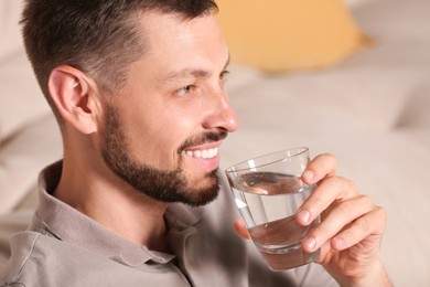 Photo of Happy man drinking water indoors, closeup. Refreshing drink