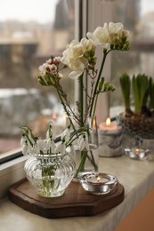 Photo of Different beautiful spring flowers and candles on windowsill indoors