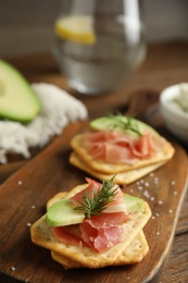 Photo of Delicious crackers with avocado, prosciutto and dill on wooden board, closeup