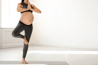 Young pregnant woman in fitness clothes practicing yoga at home. Space for text
