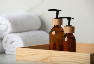 Wooden tray with dispenser bottles and towels on white table, closeup