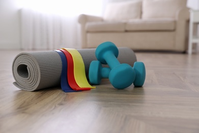 Photo of Dumbbells, elastic bands and yoga mat on floor in room, space for text. Home fitness