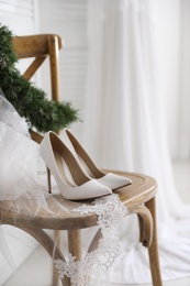 Pair of white high heel shoes, veil and wreath on wooden chair indoors. Dressing for wedding