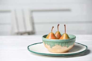 Dishware with pears on table against blurred background. Space for text