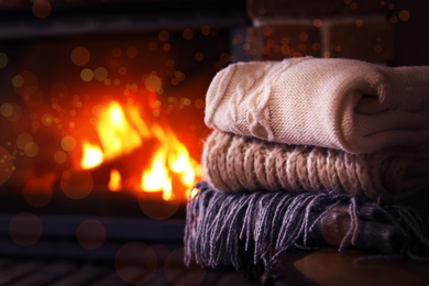 Stack of knitwear near fireplace with burning wood indoors. Winter vacation