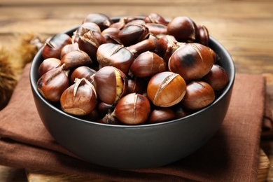 Delicious roasted edible chestnuts in bowl on table, closeup