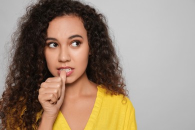 African-American woman biting her nails on grey background. Space for text