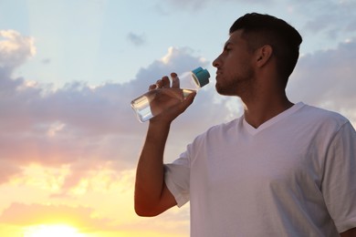 Man drinking water to prevent heat stroke outdoors at sunset, space for text