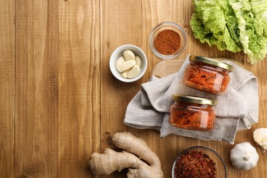 Delicious kimchi with Chinese cabbage and ingredients on wooden table, flat lay. Space for text