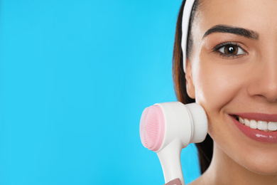 Young woman using facial cleansing brush on light blue background, closeup with space for text. Washing accessory