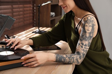 Beautiful woman with tattoos on arm using turntable at table indoors, closeup