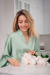 Pretty young woman in beautiful silk robe with flowers at kitchen table