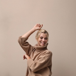 Happy woman in stylish sweater on beige background